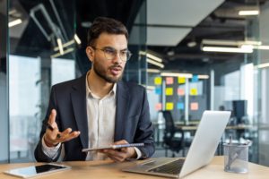 Young professional discussing business in modern office setting while using a laptop